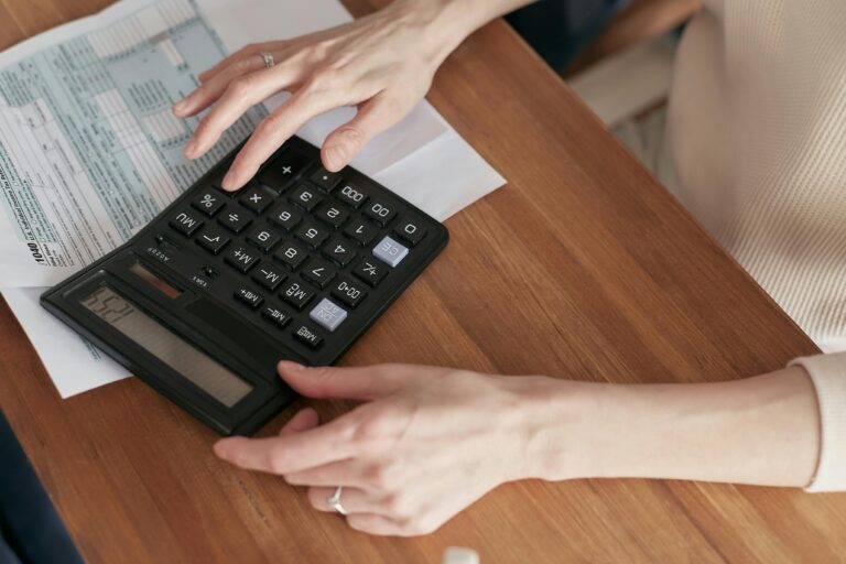 Person calculating taxes with calculator and tax forms on wooden desk, personal tax preparation.