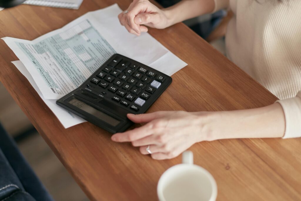 Person calculating expenses with a calculator and NDIS-related documents, illustrating financial planning and support participants can expect from a plan manager in 2026.