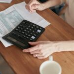 Person calculating expenses with a calculator and NDIS-related documents, illustrating financial planning and support participants can expect from a plan manager in 2026.