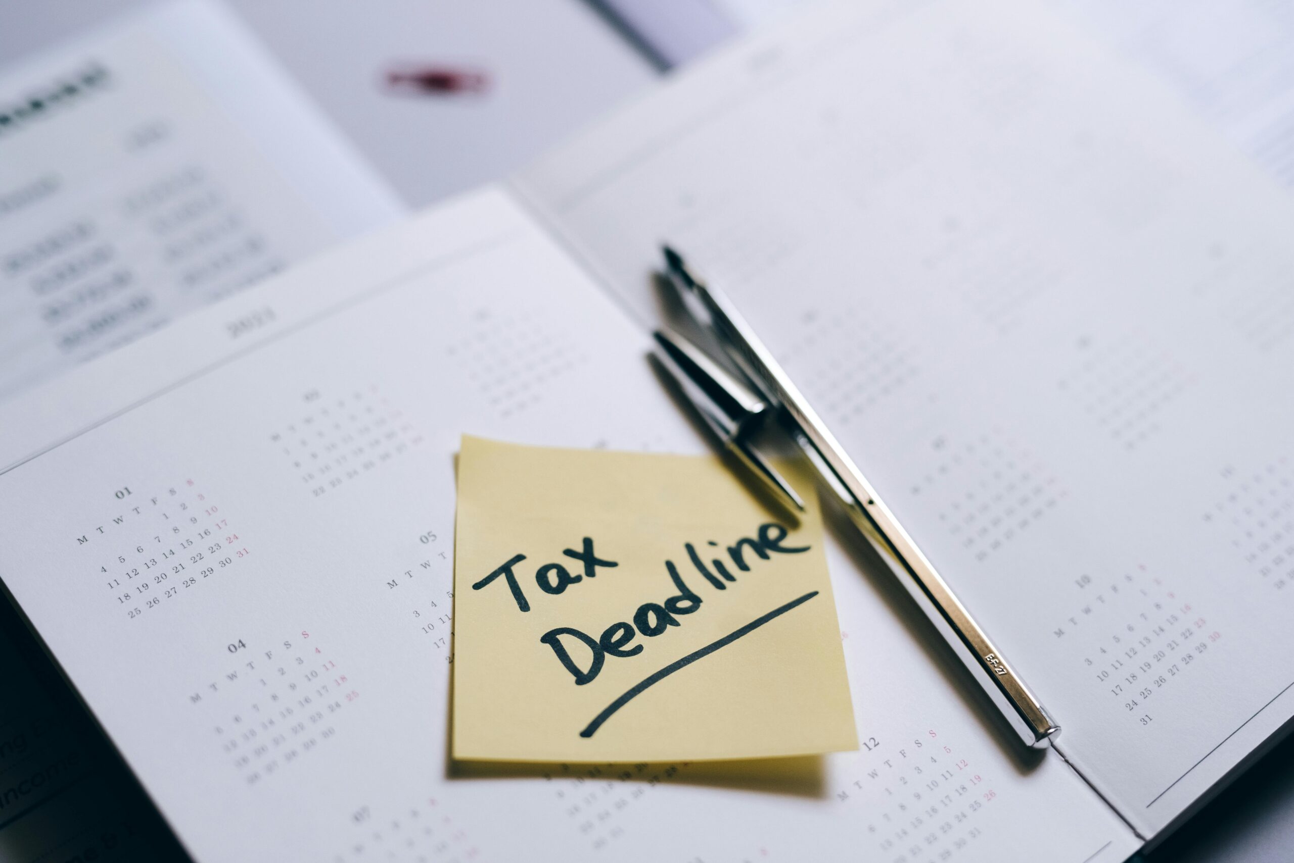 Tax deadline reminder written on sticky note placed on calendar with pen, tax planning concept.